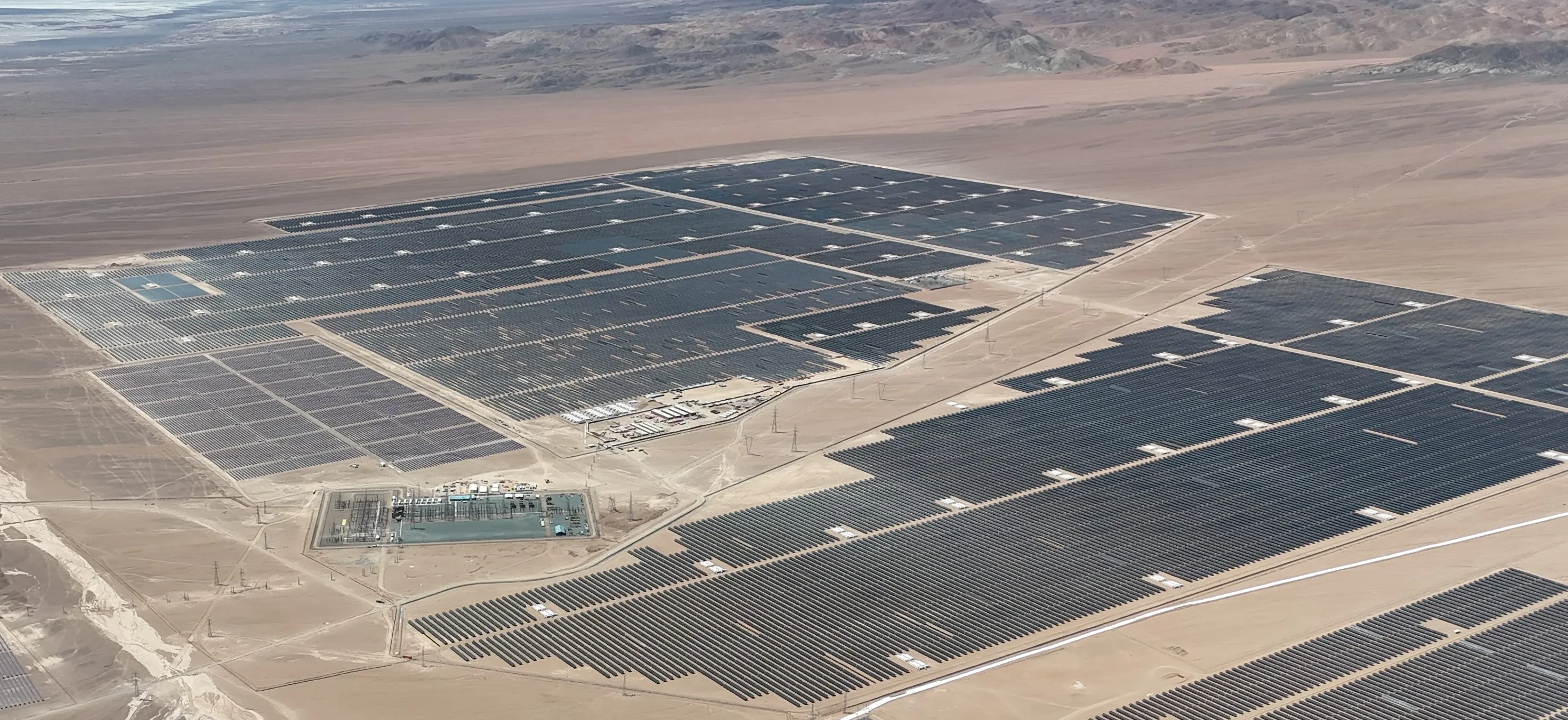 Aerial view of the AES Andes solar facility in Chile featuring extensive rows of photovoltaic panels across a desert landscape with supporting electrical infrastructure.